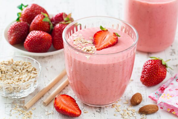 A glass of strawberry smoothie with strawberries on the side.